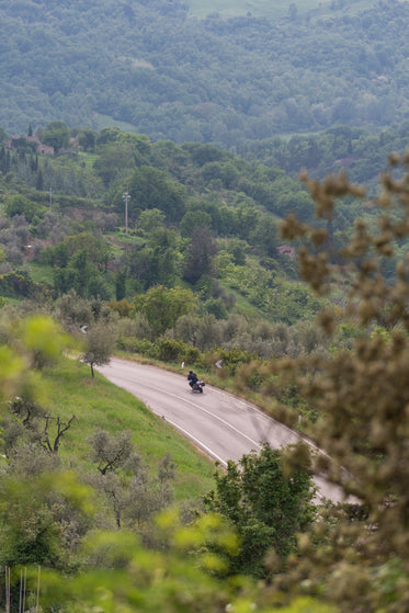 a motorcycle takes a curve on a highway around a hill