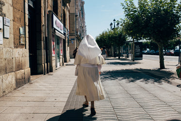 a nun in a white habit strolls a sunny pedestrian walk
