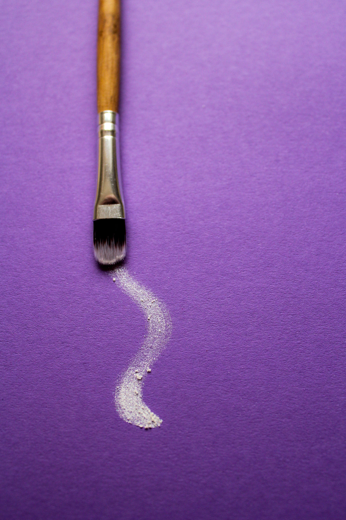 a paintbrush trails white paint on purple paper