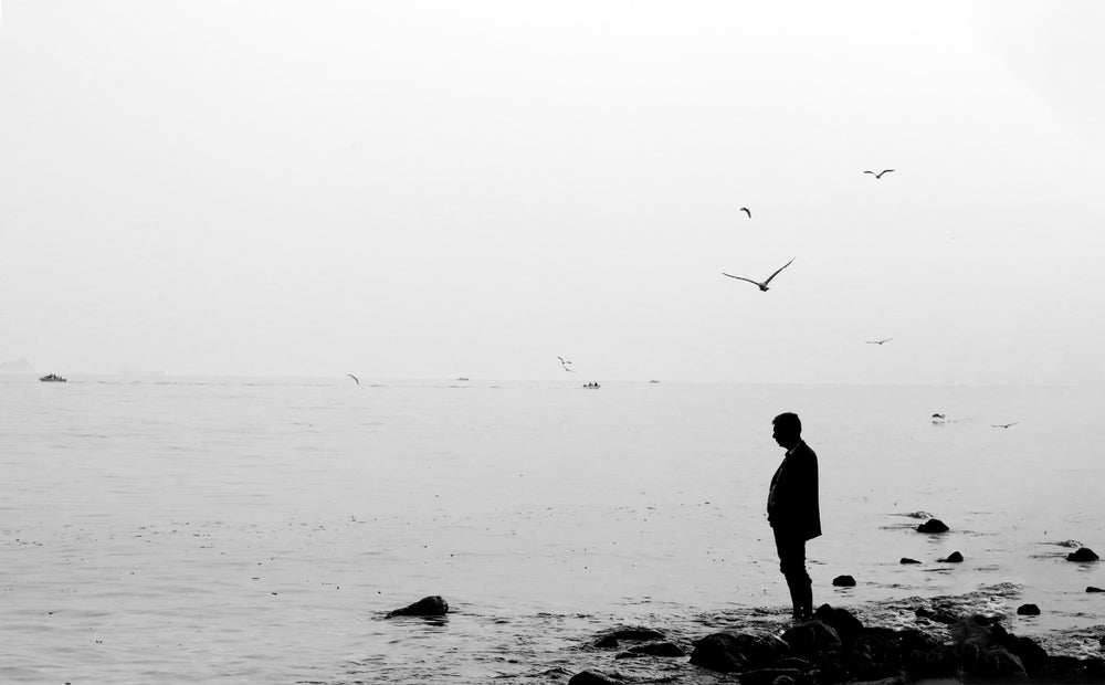 a person standing on rocks by still water in black and white