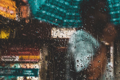 a person with an umbrella through a rain-speckled window