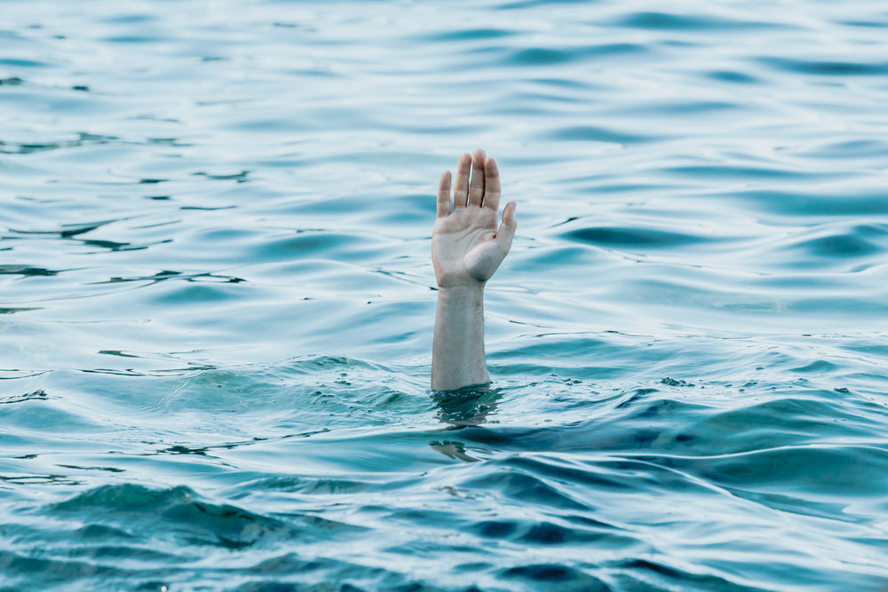 a persons hand reaches out toward the blue water