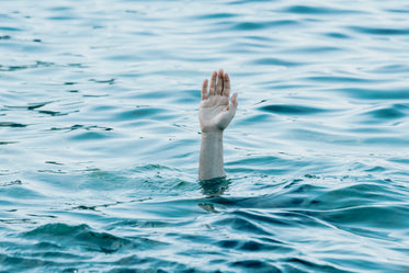 a persons hand reaches out toward the blue water