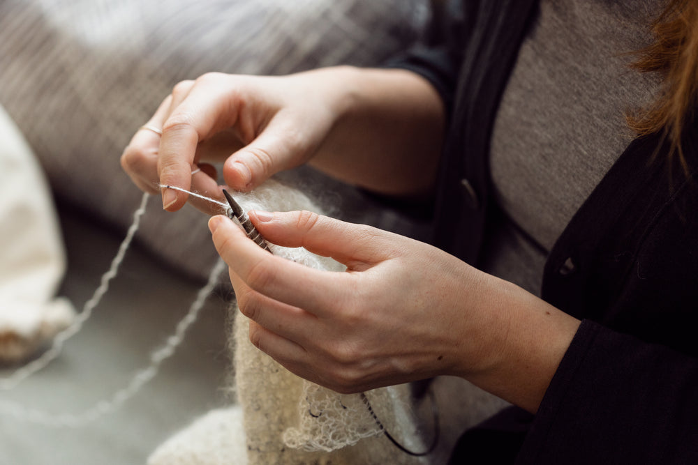 a persons hands knitting with white wool