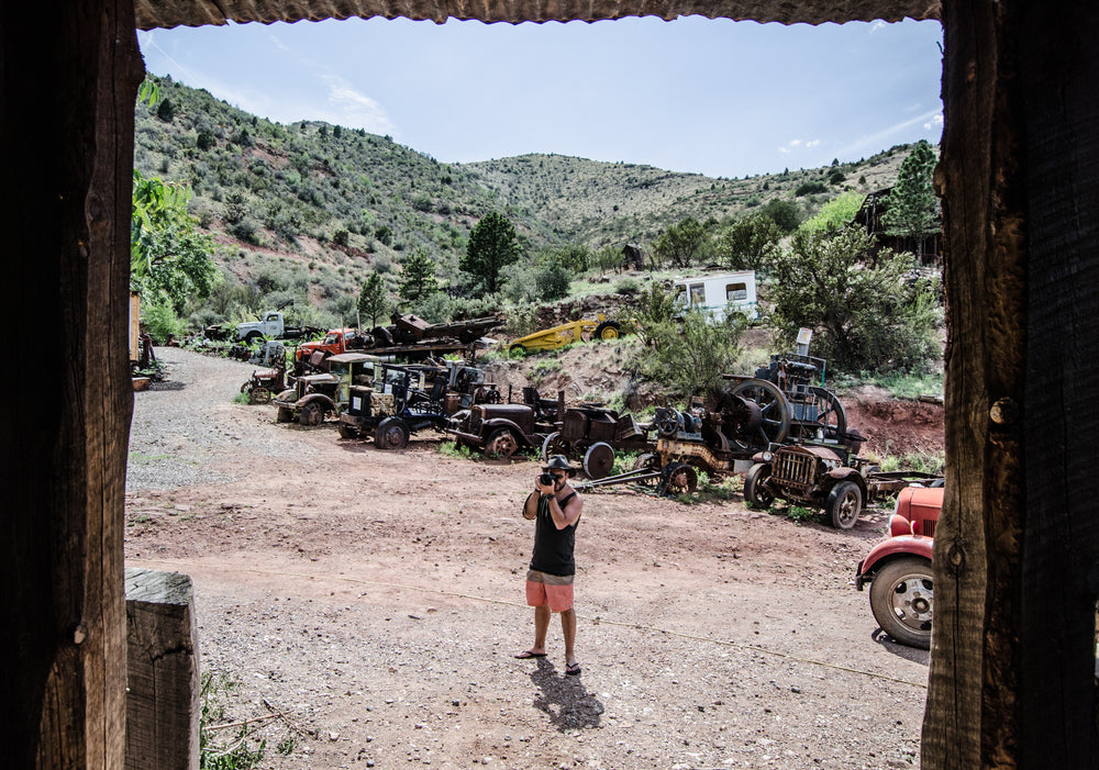 a photographer in a desert graveyard of cars snaps a photo