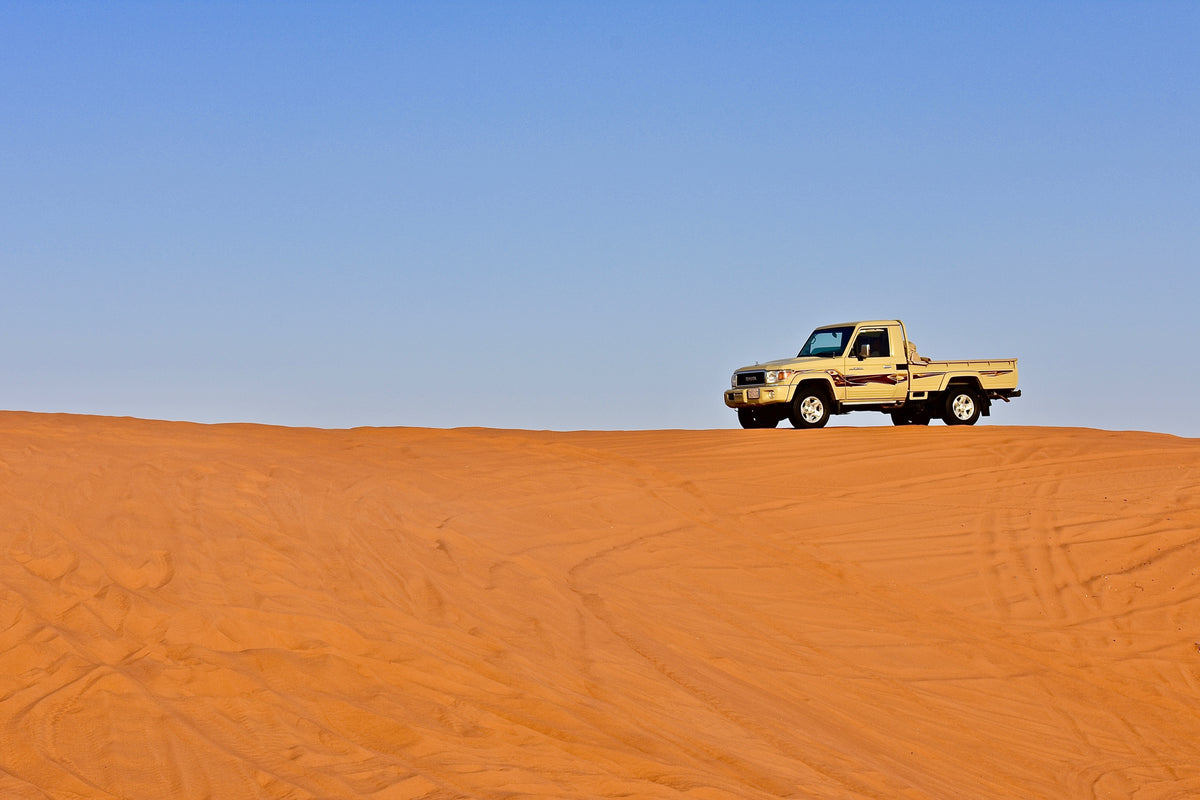 a pick-up truck on the desert dunes under a blue sky