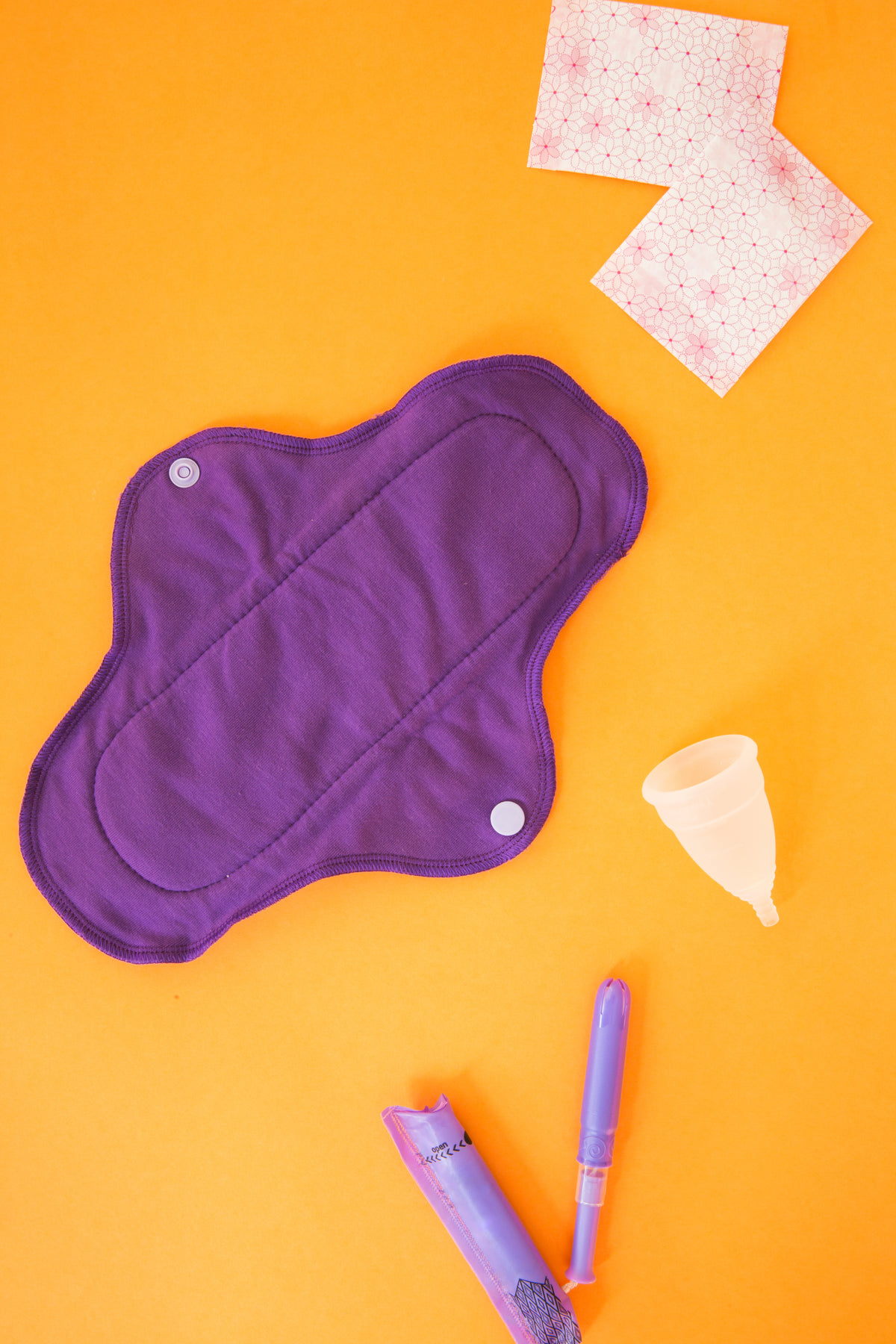a purple reusable menstrual pad, cup and applicator