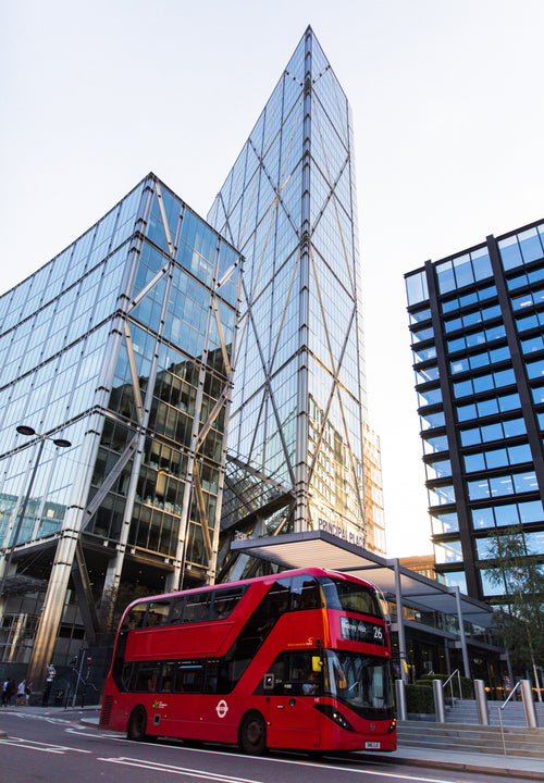 a red bus drives under glassy skyscrapers