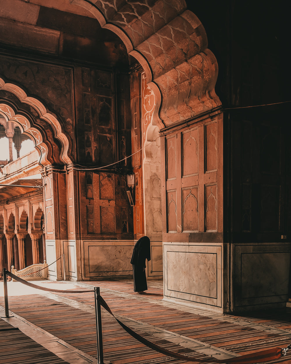 a robed figure walks through arches