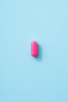 a single pink pill on a baby blue surface