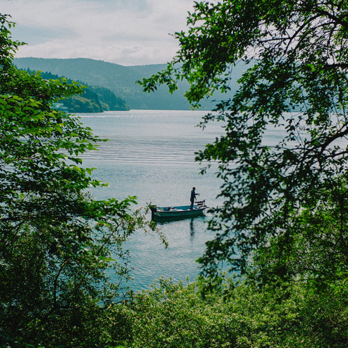A Small Fishing Boat In Still Water Through Lush Trees