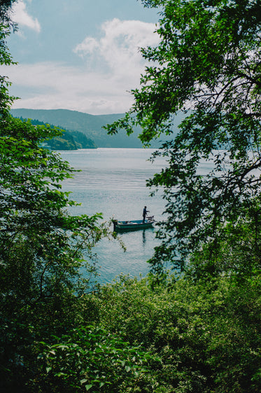 a small fishing boat in still water through lush trees