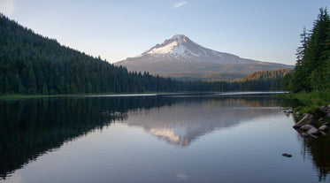 a snow-capped mountain overlooks a lake lined with trees