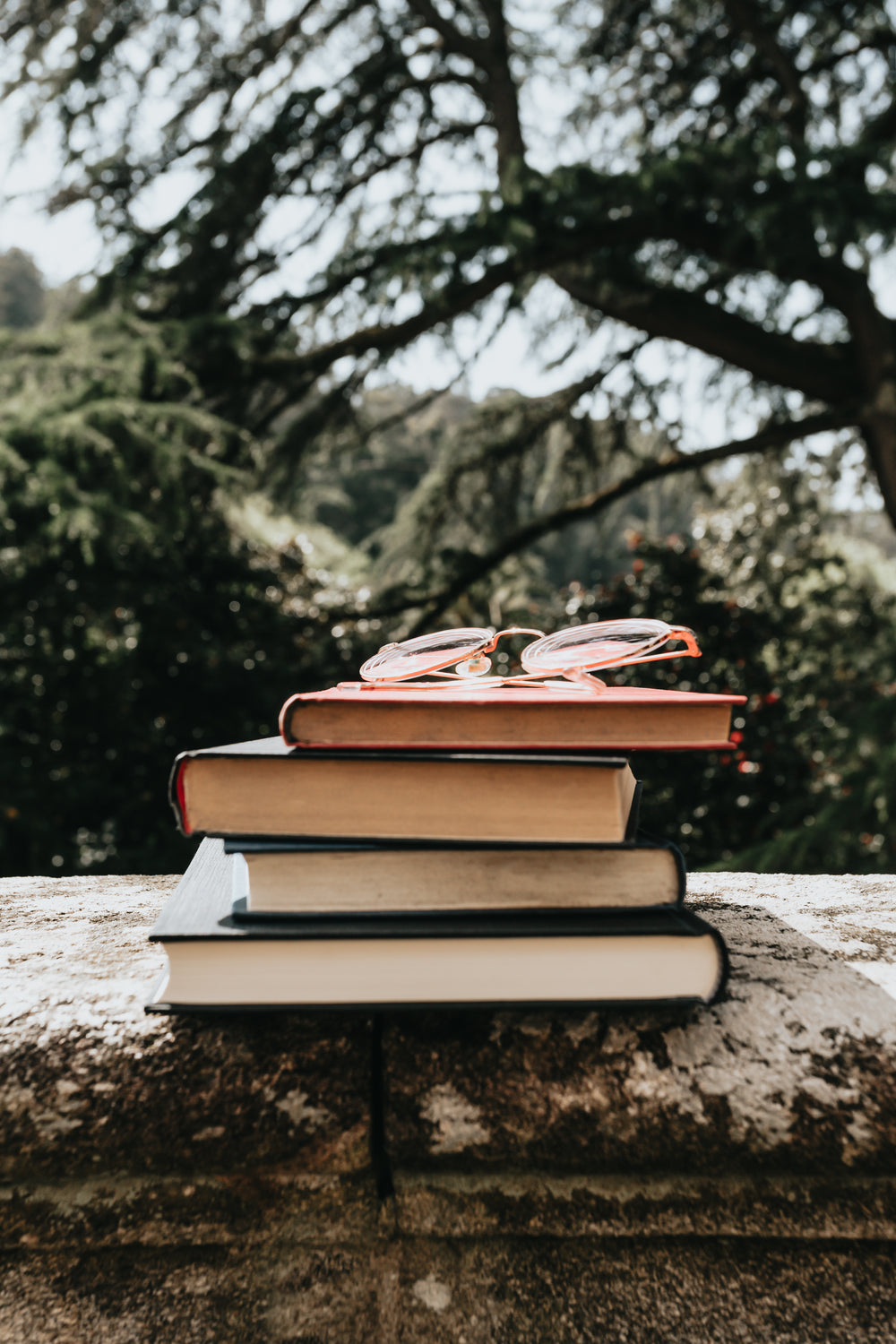 a stack of hardcover books outdoors with glasses