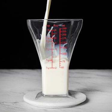 a stream of milk pours into triangle-shaped measuring glass