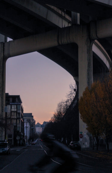 a sun sets behind city buildings from under bridge