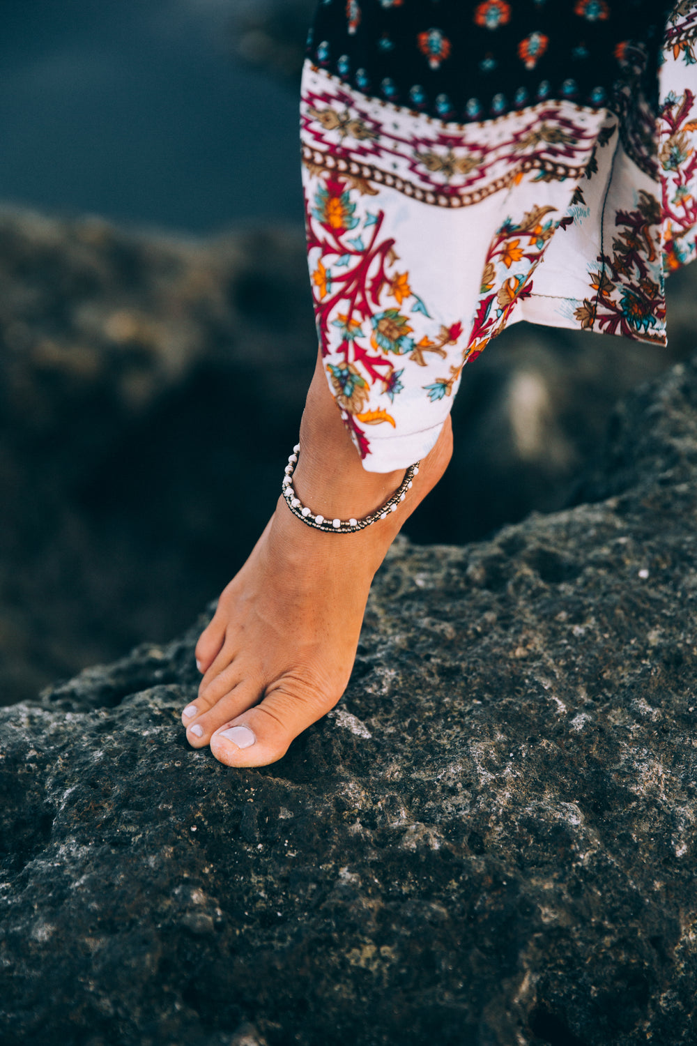 a tanned woman exhibits anklet on rocky seashore