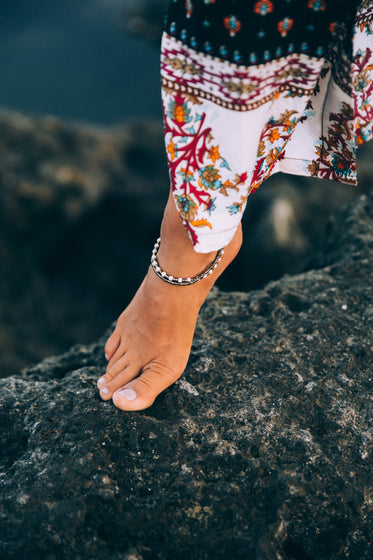 a tanned woman exhibits anklet on rocky seashore