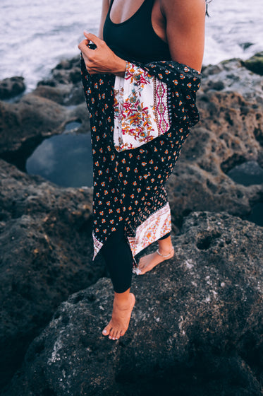 a tanned woman with patterned shawl poses on beach