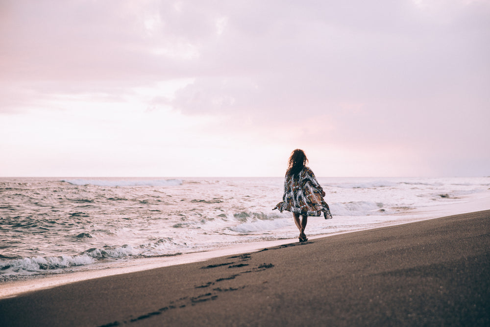 a tanned women in flowing beach robe walks along the beach