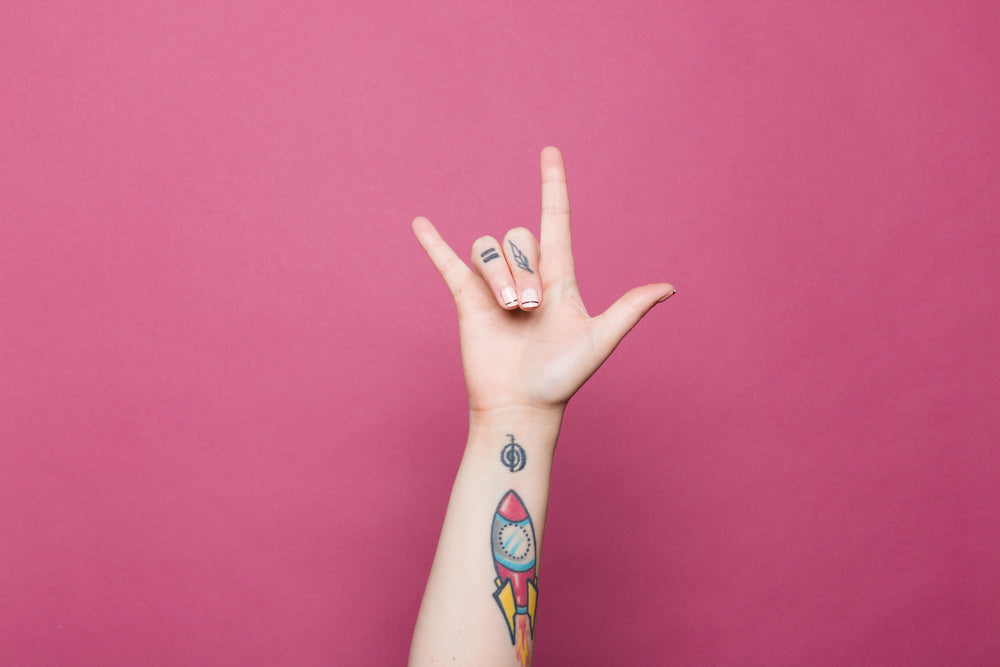 a tattooed hand doing the sign for i love you