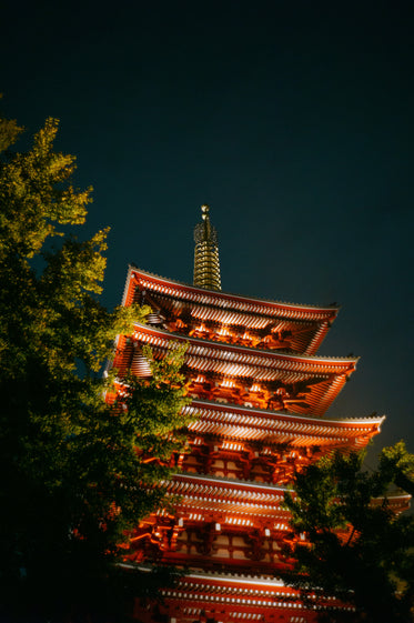 a view through green trees of building in red lights