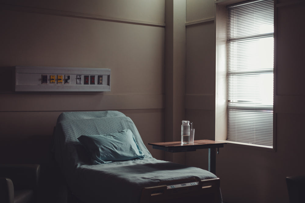 uma jarra de água e um copo sobre uma mesa perto de um leito de hospital