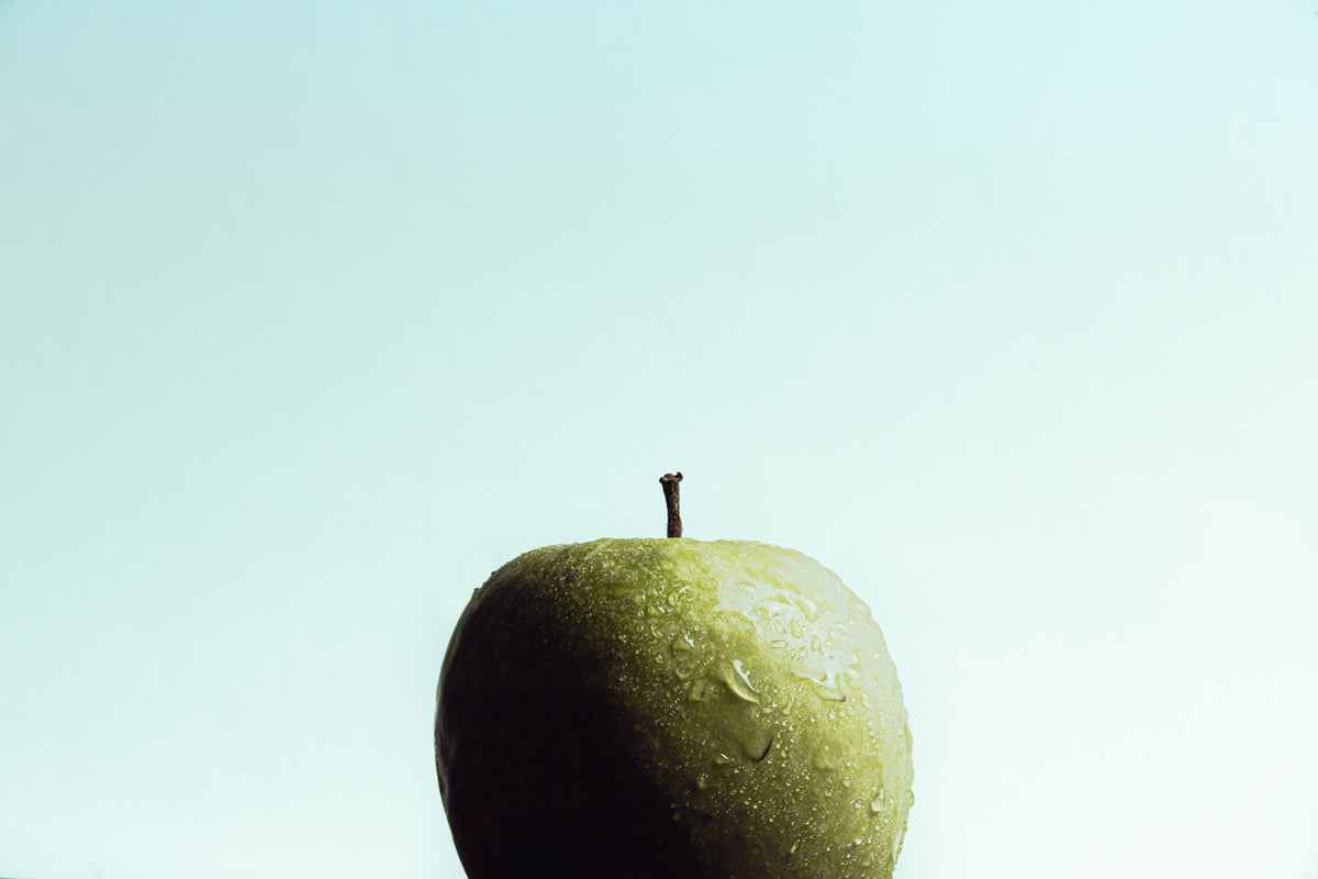 a wet crisp green apple against a light blue background