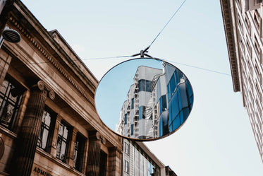 a white building is reflected in a large traffic mirror