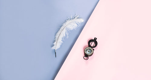 a white feather quill and compass on pink and purple