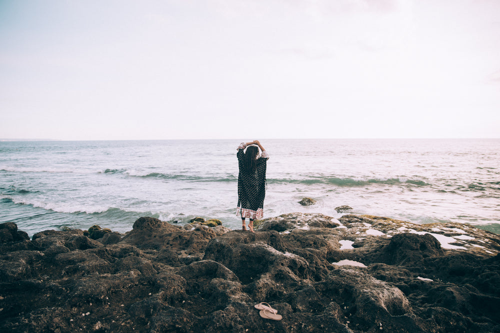 a woman by the beach holds her hands up in reverie