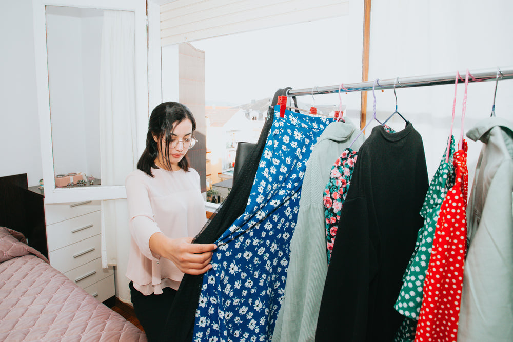 a woman holding a dress browses her bedroom clothing rack