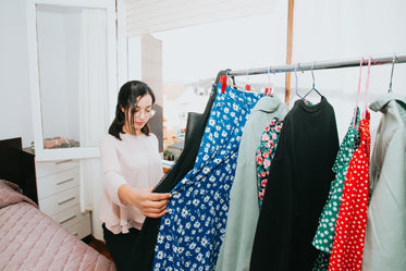 a woman holding a dress browses her bedroom clothing rack