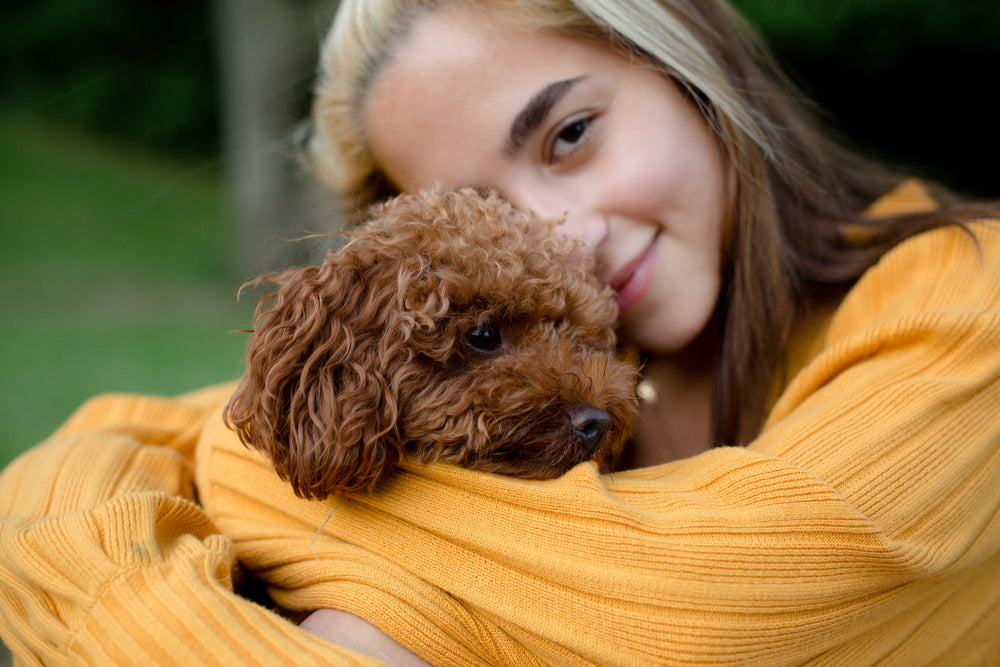 a woman hugs a small brown puppy outdoors