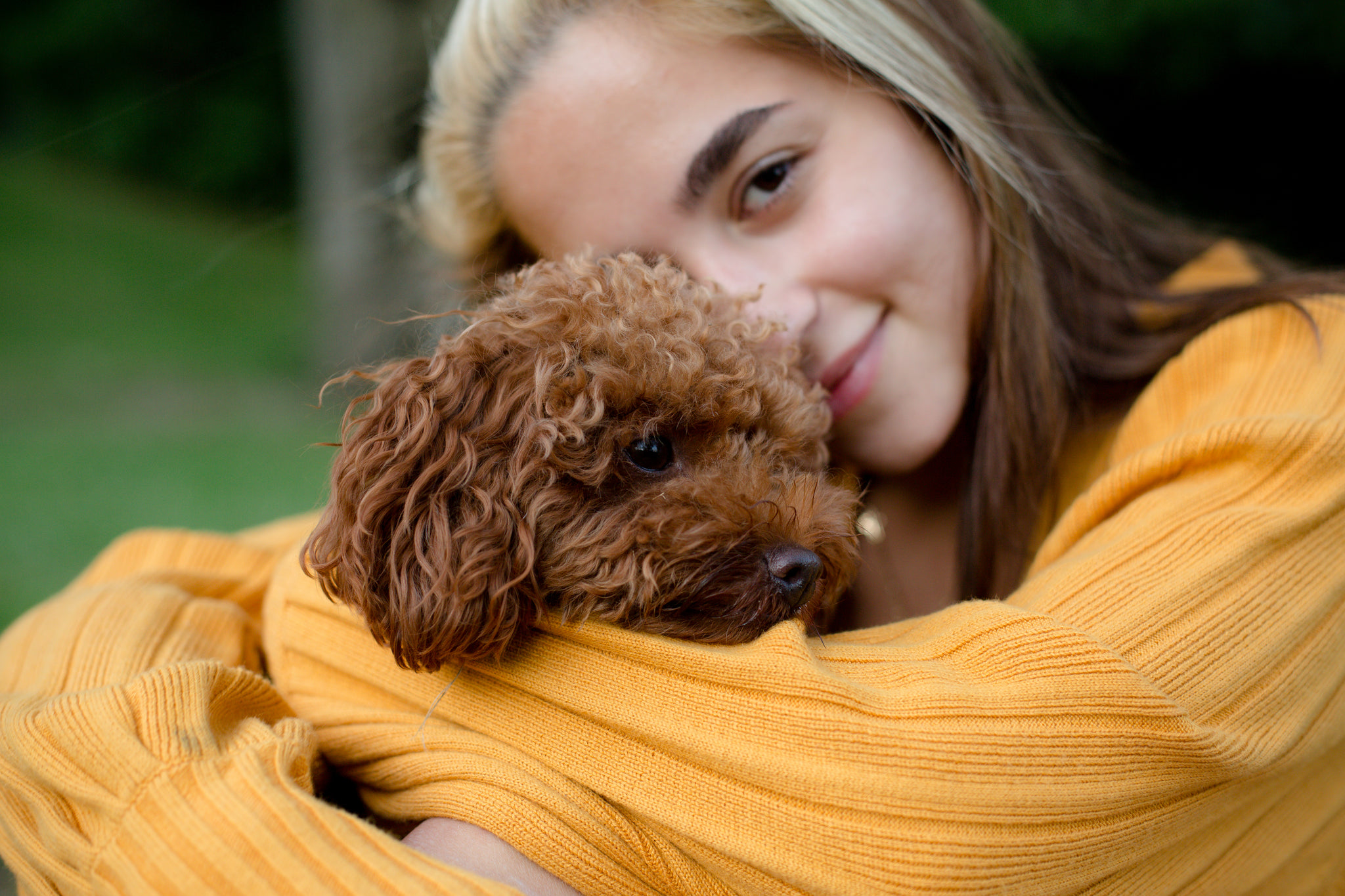 A Woman Hugs A Small Brown Puppy Outdoors