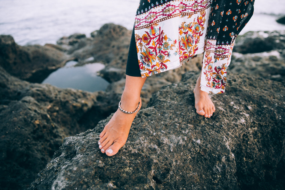 uma mulher com vestido florido caminha na praia com pés descalços