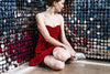 a woman in a red dress sits and ponders a wall of mirrors