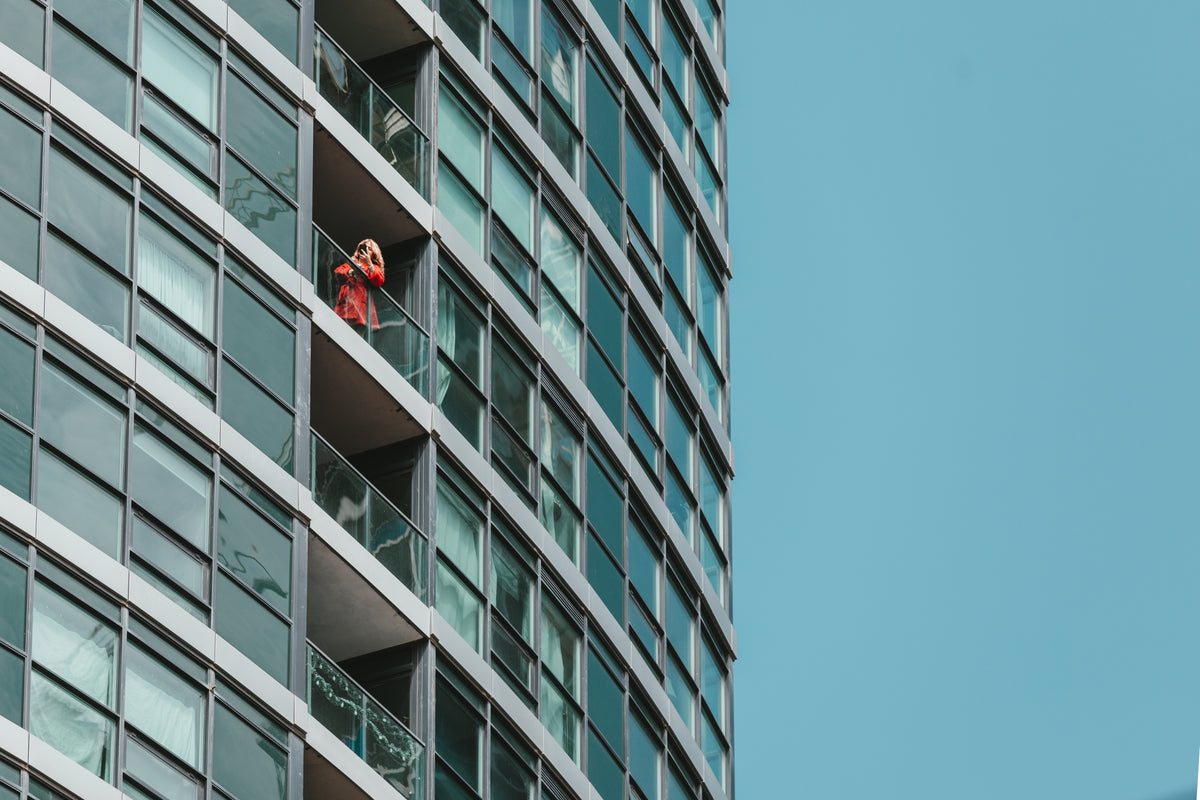 a woman in a red jacket inspects her phone on a balcony