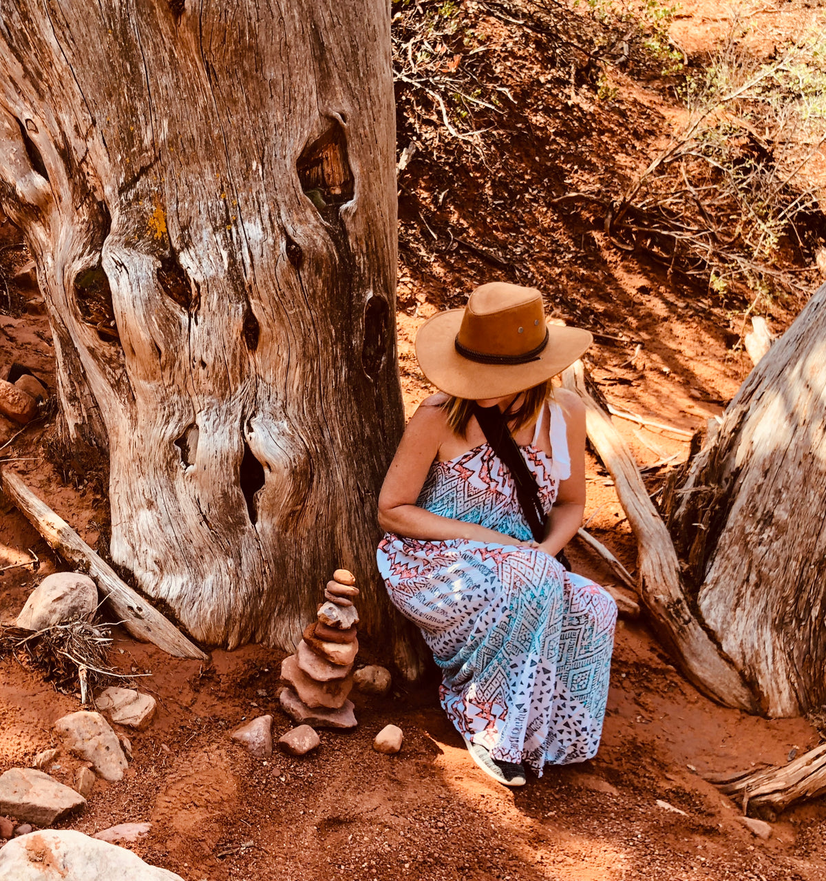 a woman in cowboy hat crouches by a tree in the desert