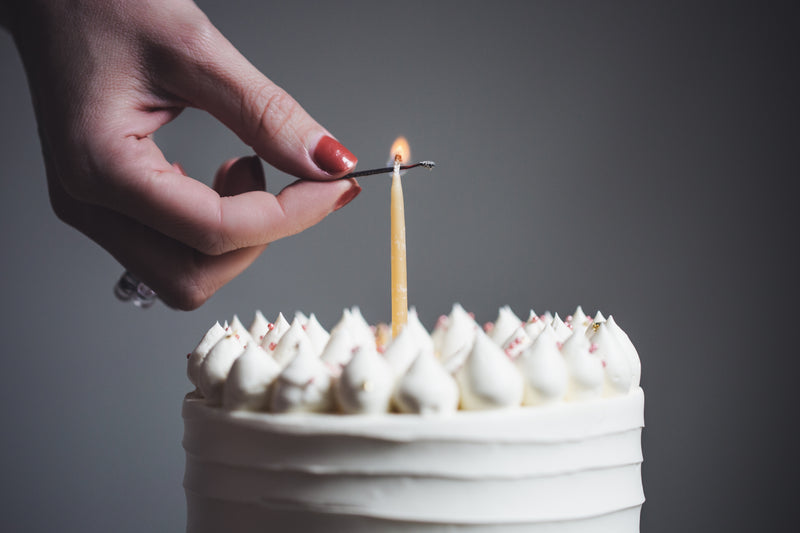 a woman lits a single birthday candle - a person lighting a candle on a cake