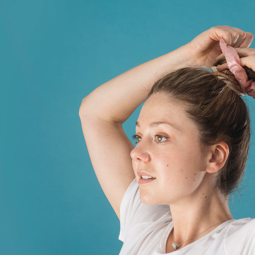 A Woman Putting Her Hair Up With A Pink Scrunchie