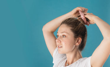 a woman putting her hair up with a pink scrunchie