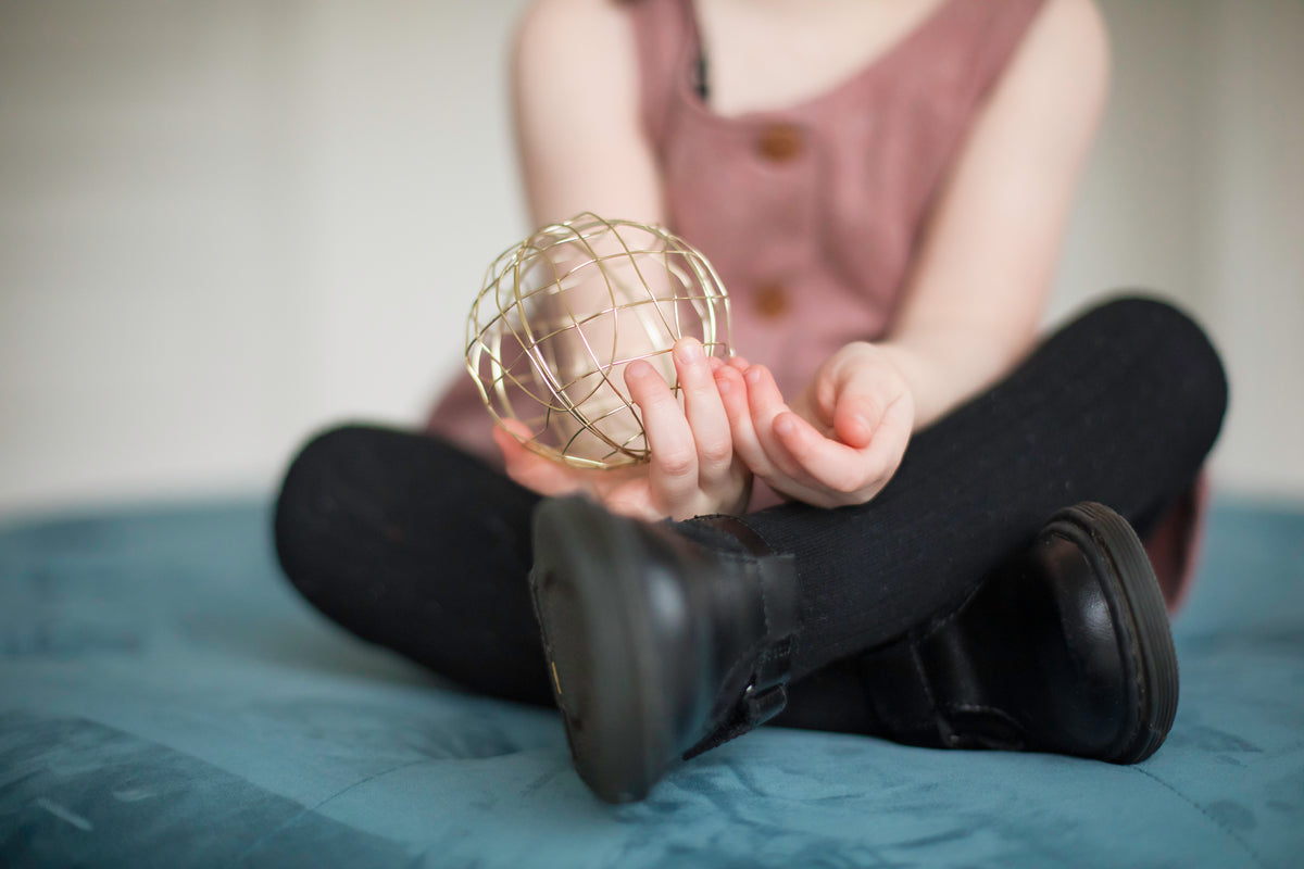 a woman sat on a bed holds out a gold mesh ball