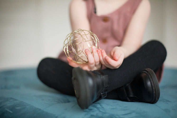 A Woman Sat On A Bed Holds Out A Gold Mesh Ball