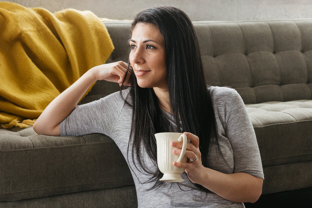 mulher sentada tomando café aos pés do sofá