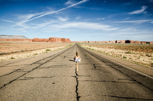 a woman sits in the middle of a desert highway
