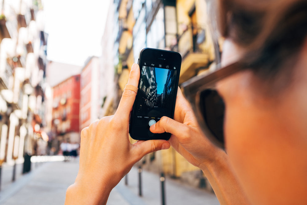 a woman snaps a photo on her mobile phone up a sunny street