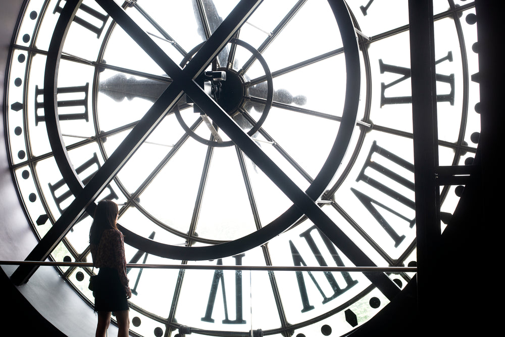 a woman stands at the back of a massive white clock face