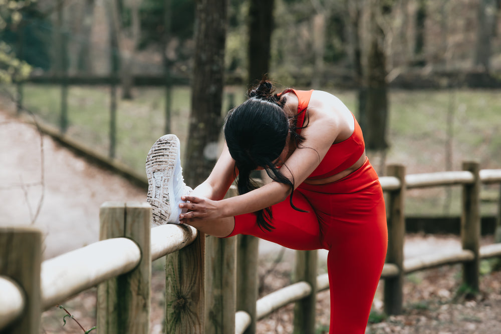 a woman stretches outdoors against a wooden fence