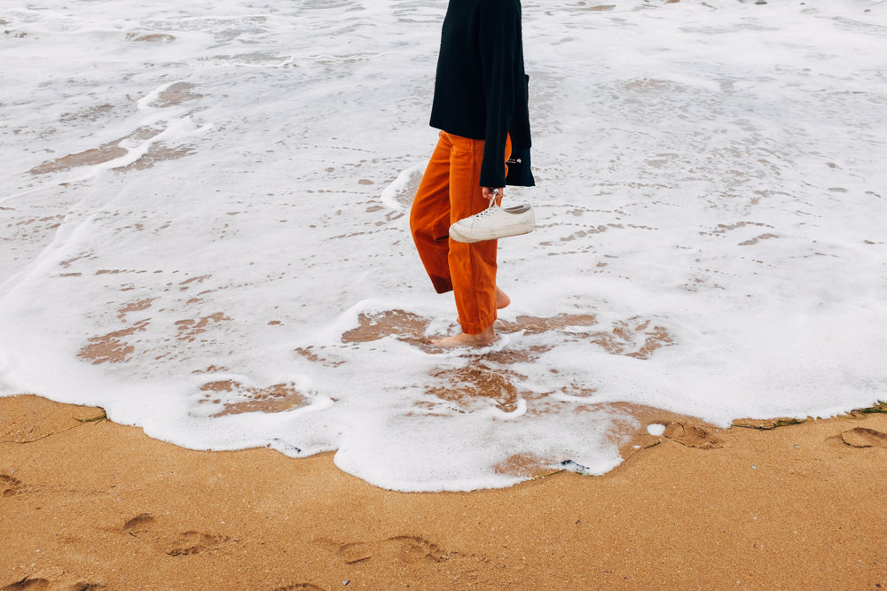 mulher caminha descalça pela beira da água na praia